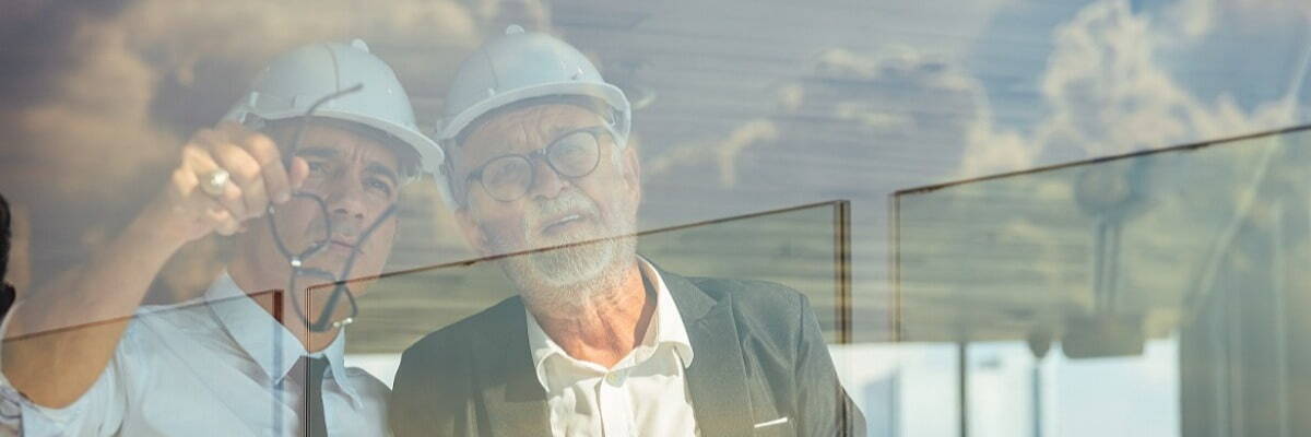 Two men in hard hats looking out a window and talking