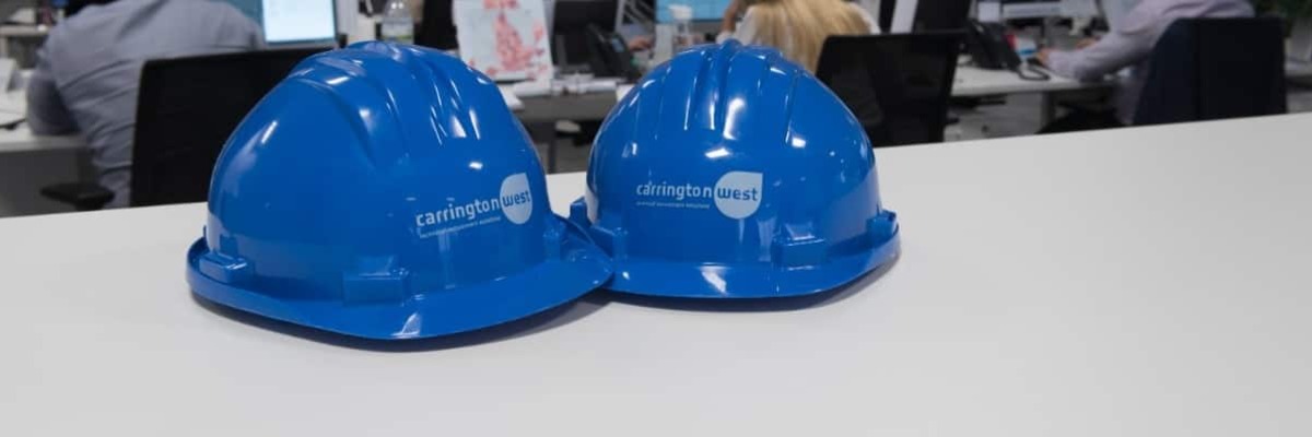 Two Carrington West branded hard hats on an office desk